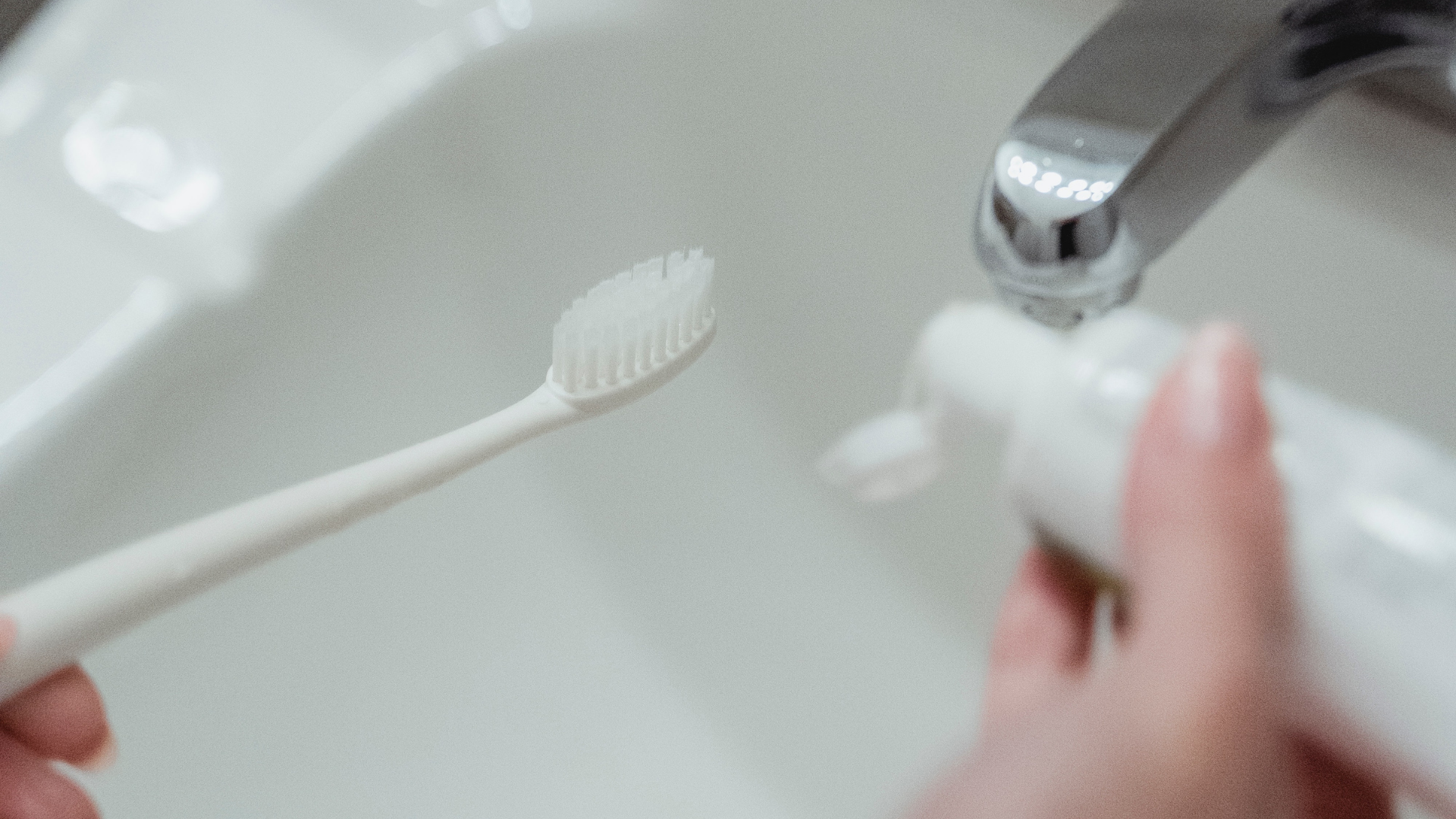 hand holding toothbrush by faucet